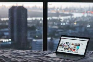 Laptop with WordPress image gallery opened on it on a bed next to a large window overlooking a city.