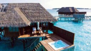 Two people lying on sunbeds and working on their laptops in front of a bungalow in the Maldives.