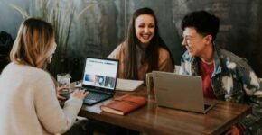 Three smiling young people sitting with laptops