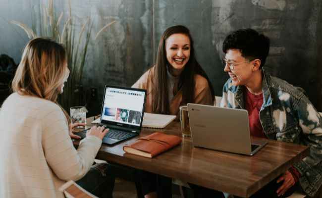 Three smiling young people sitting with laptops