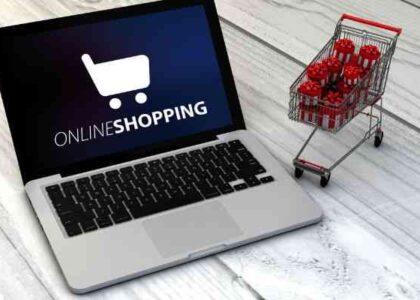 A laptop showing online shopping on screen and a shopping cart beside the laptop