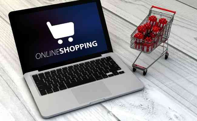 A laptop showing online shopping on screen and a shopping cart beside the laptop